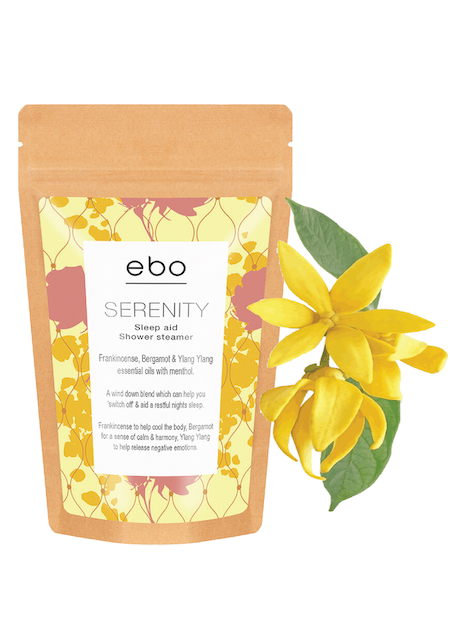 A packet of ebo serenity shower steamers next to a beautiful yellow ylang ylang flower. 