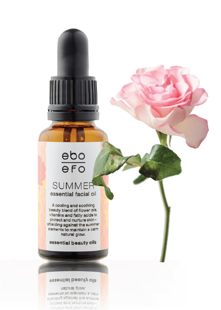 A bottle of ebo summer facial oil next to a delicate pink rose. 
