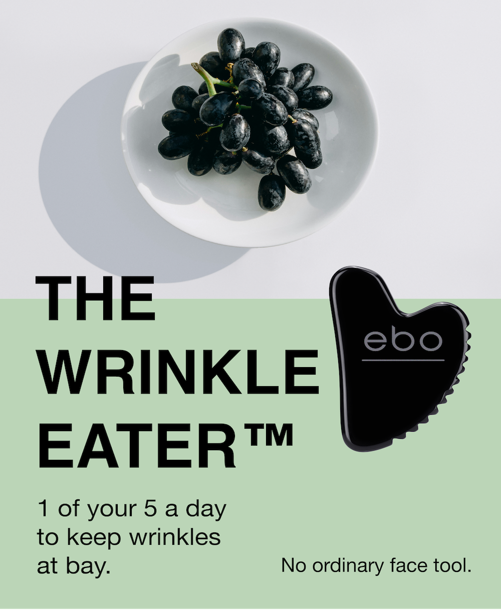 A bowl of black grapes on a white background next to an image of black, obsidian The Wrinkle Eater TM next to a green background with black text overlayed: The WRINKLE EATER TM. 1 of your 5 a day to keep wrinkles at bay. No ordinary face tool. 